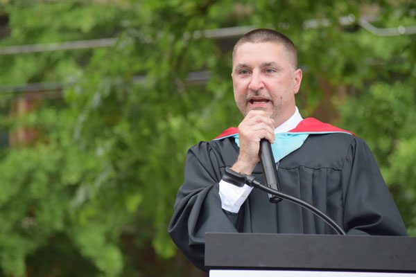 Adult in graduation robe speaking at a podium.