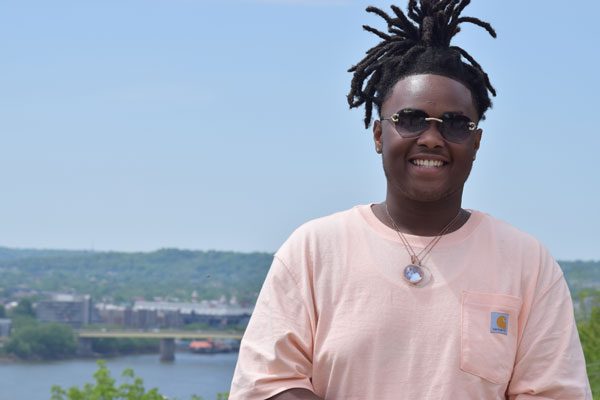 Smiling adult with dreadlocks and sunglasses outdoors.