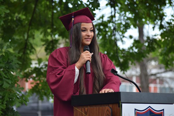 Adult in graduation attire speaking at a podium.