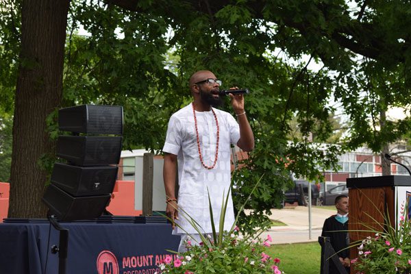 Adult speaking into microphone at an outdoor event.