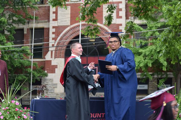Adults shaking hands at graduation, one receiving a diploma.