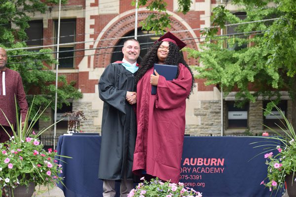 Two adults in graduation attire shaking hands.