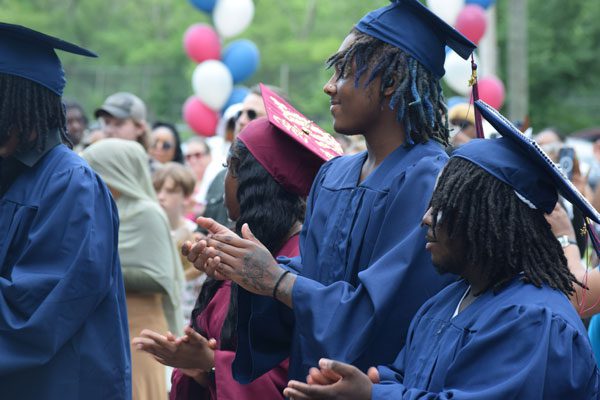 Graduates in caps and gowns clapping during a ceremony.