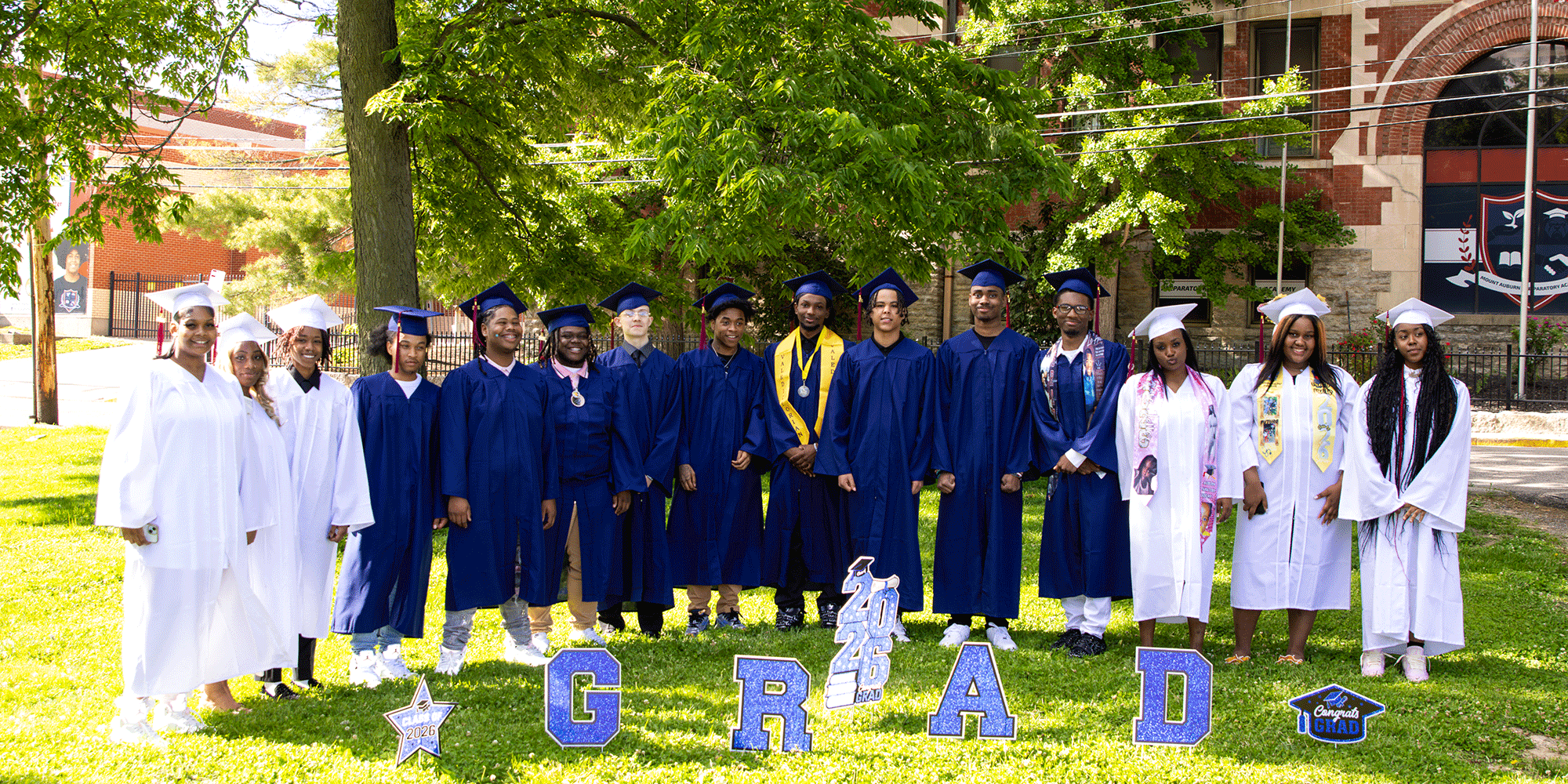 Adults in graduation caps and gowns pose with "GRAD" letters.