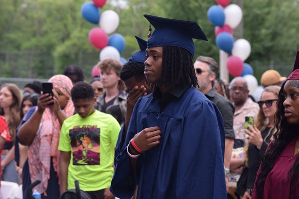 Young adult in blue graduation cap and gown in a crowd.