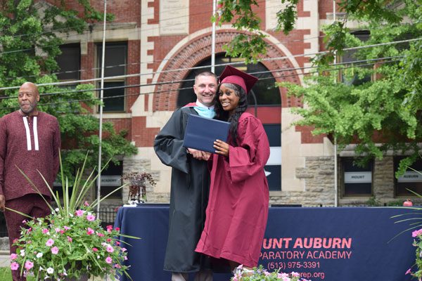 Two people in graduation attire smiling with a diploma.