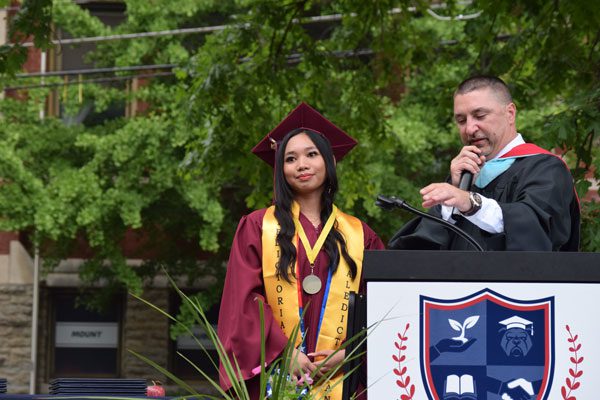 Speaker at podium next to graduate in cap and gown.