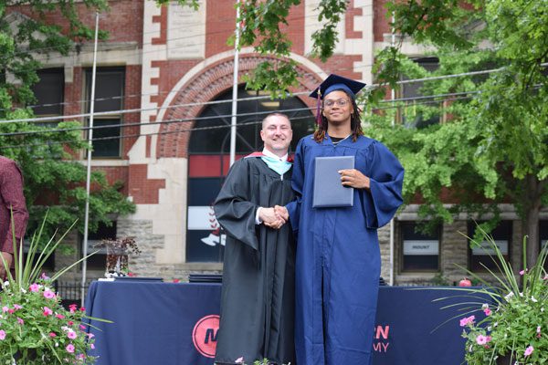 Adult and student in graduation attire shaking hands.