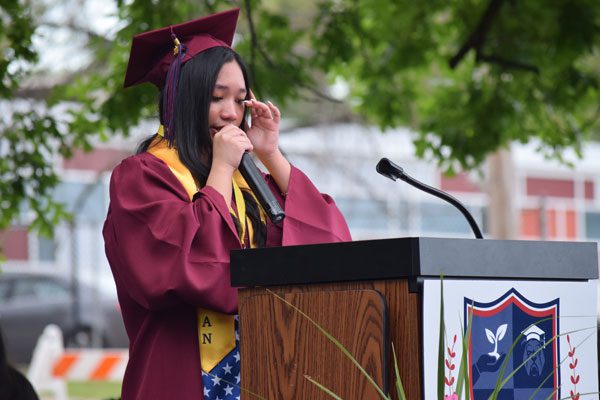 Young adult in graduation attire crying at a podium.