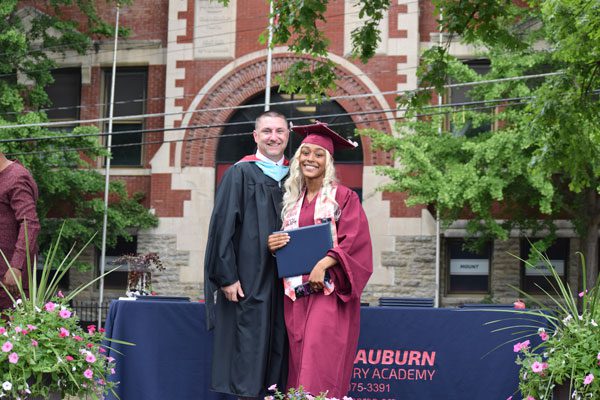 Two smiling adults in graduation attire with a diploma.