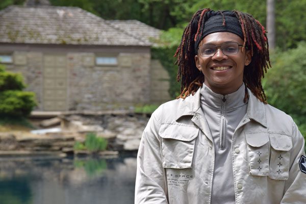 Smiling adult with dreadlocks and glasses outdoors.