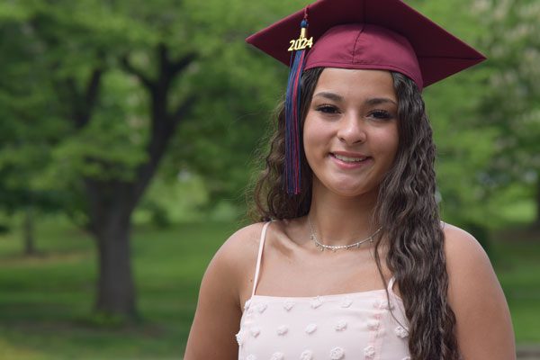 Smiling young adult in maroon graduation cap with "2024" charm.