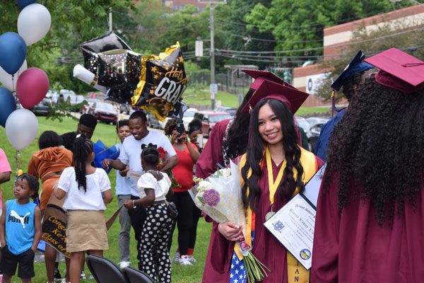 Smiling graduate in cap and gown holding diploma and flowers.