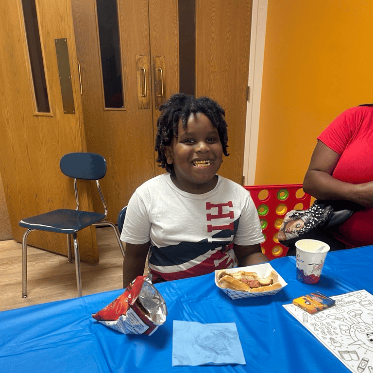 Smiling child at a table with a hot dog and chips.