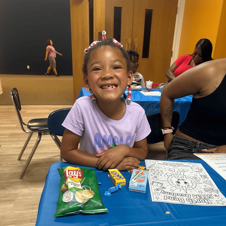 Smiling child at a table with snacks and a coloring page.