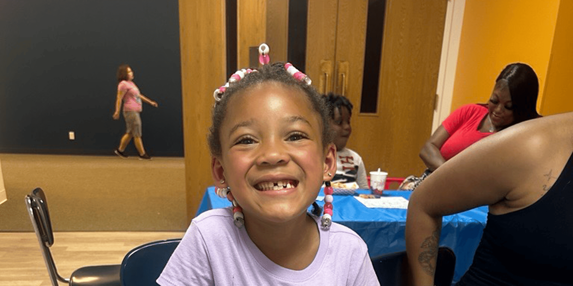 Smiling child with beaded braids looking at the camera.