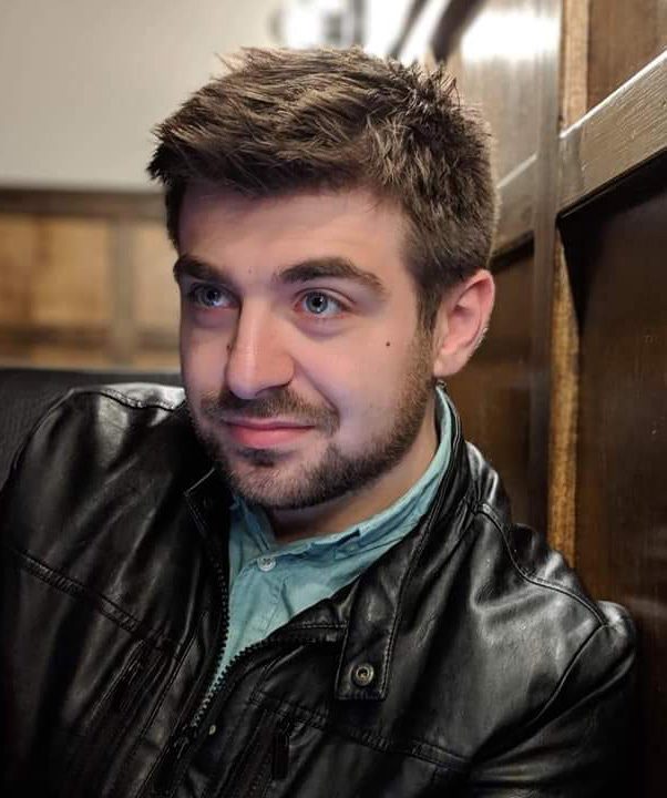 Adult in black jacket and light blue shirt.
