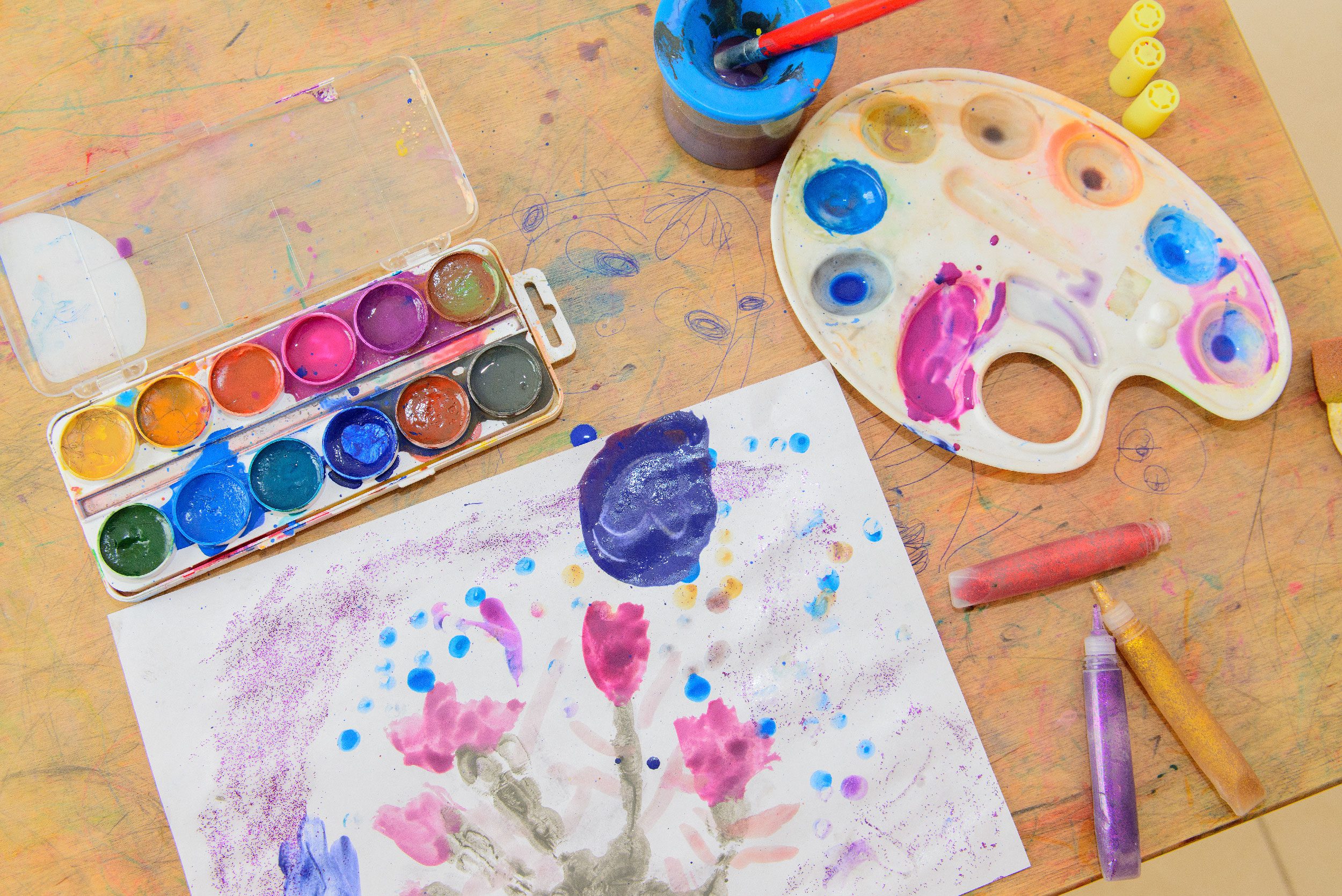 Art supplies and a child's painting on a wooden table.