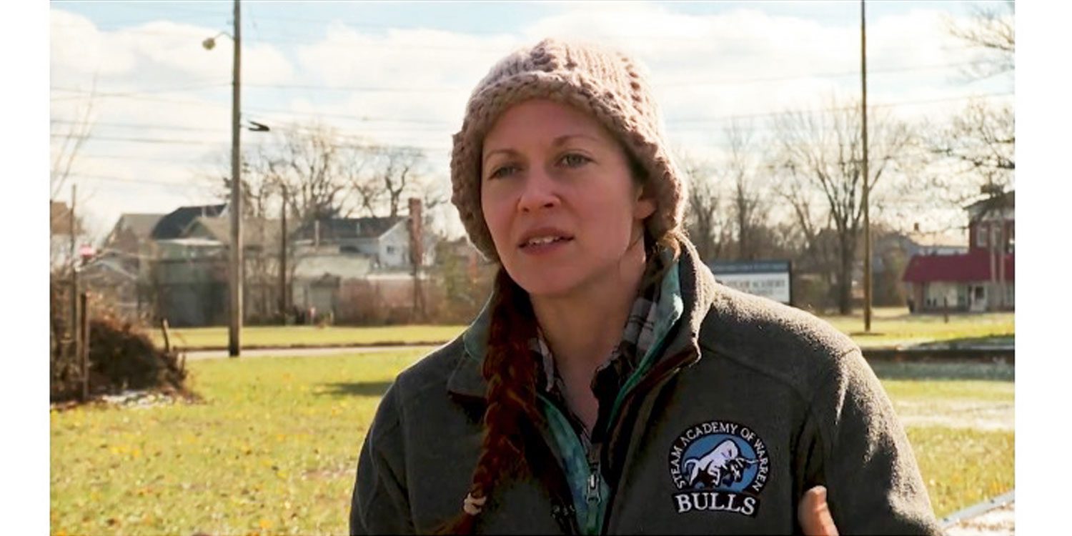 Adult in knitted hat and jacket with school logo.
