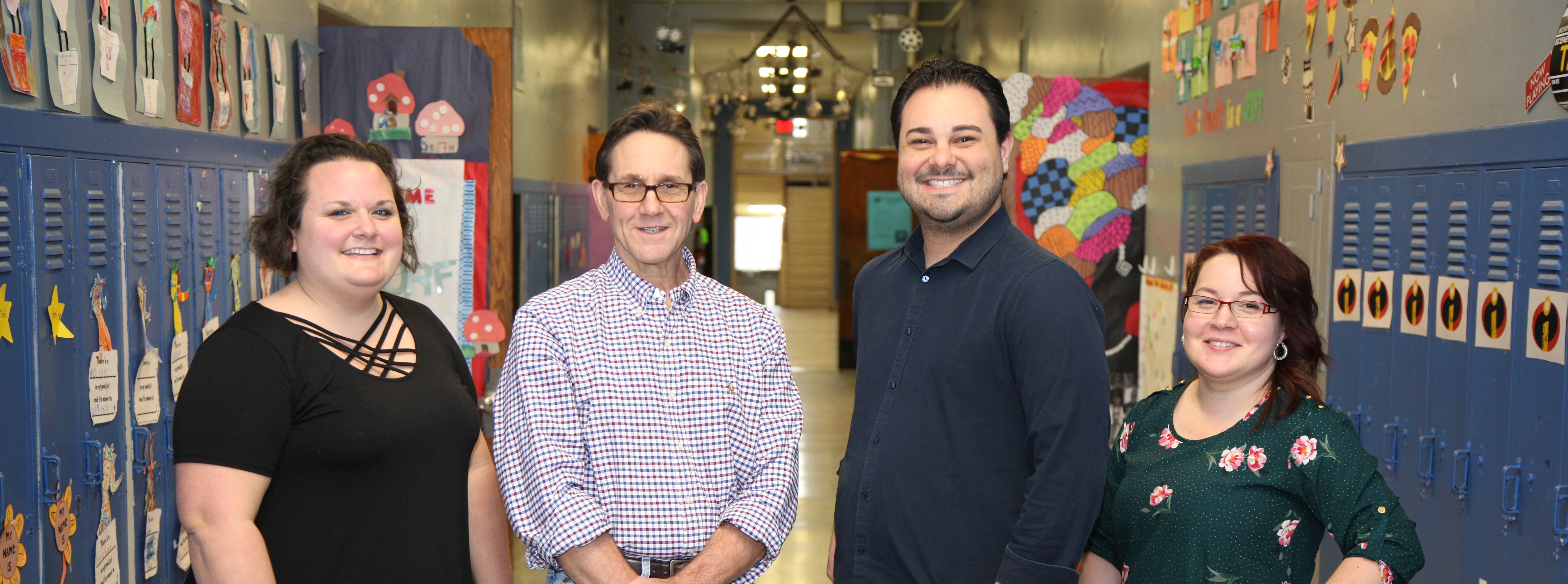 Four smiling adults in a school hallway.