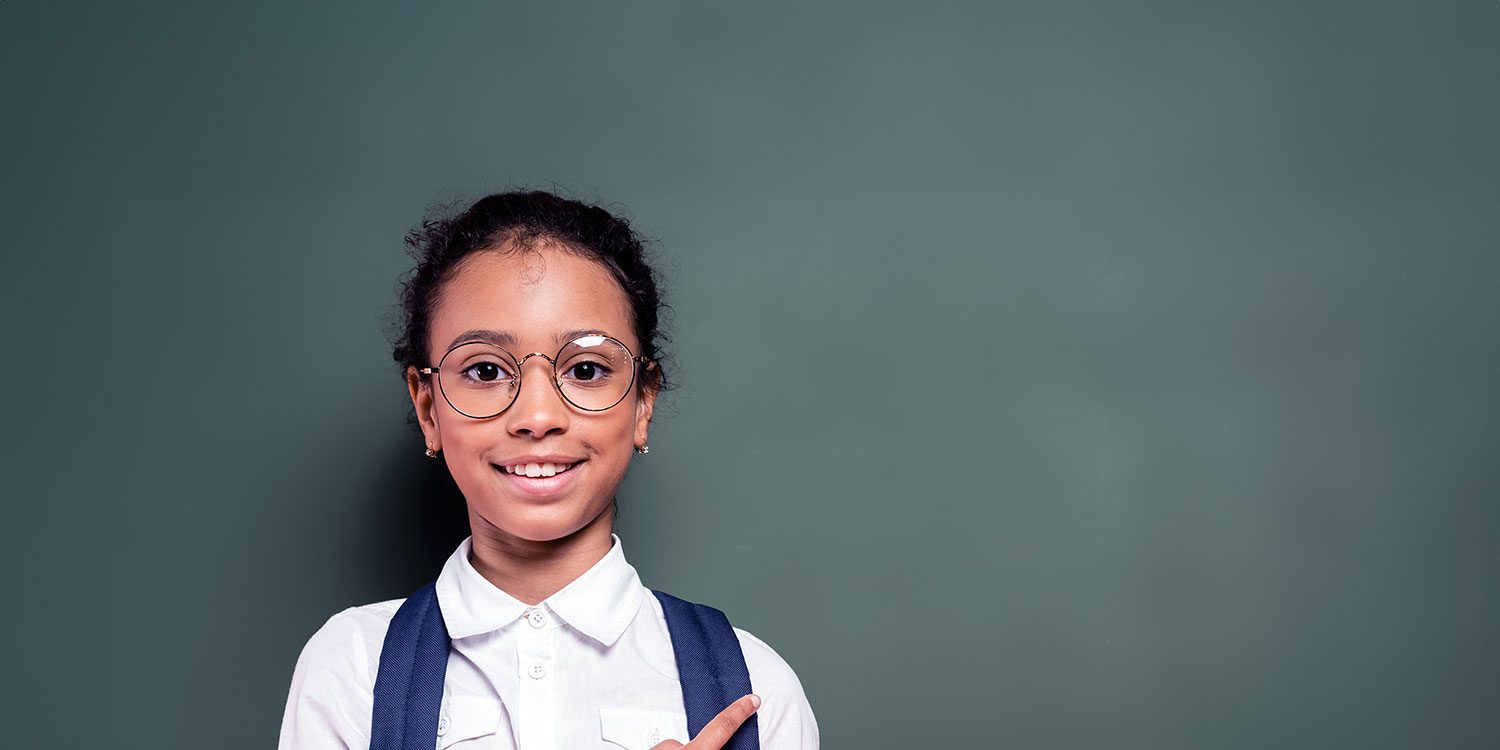 Smiling child in glasses points right, against a green background.
