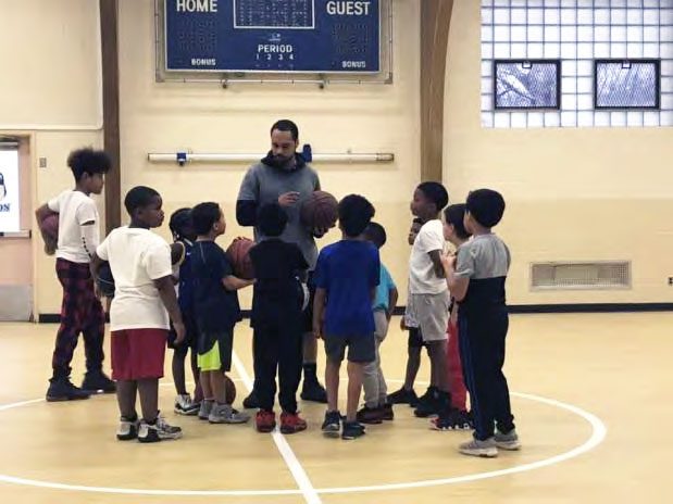 Adult and children with basketballs in a gym.