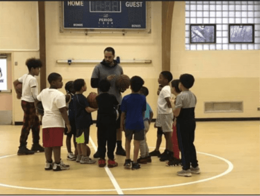 Adult and children on basketball court with basketballs.