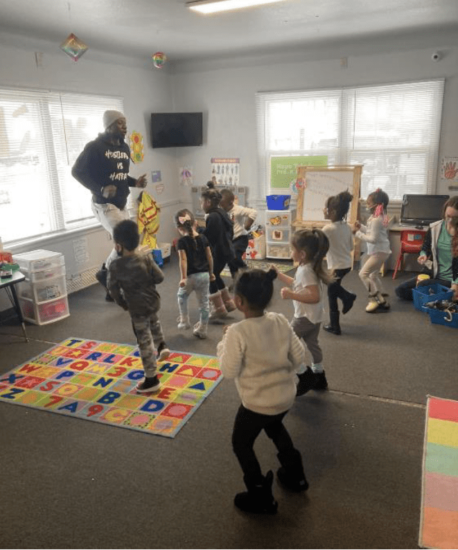 Adult and children dancing together in a classroom.