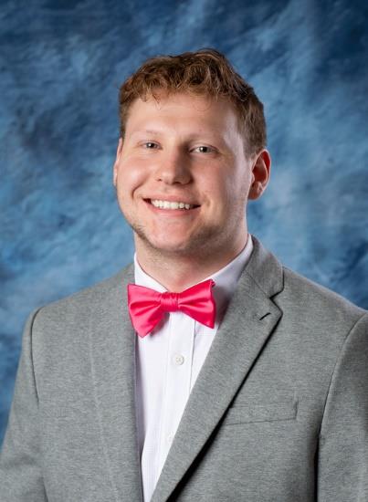 Smiling adult male in gray jacket and pink bow tie.