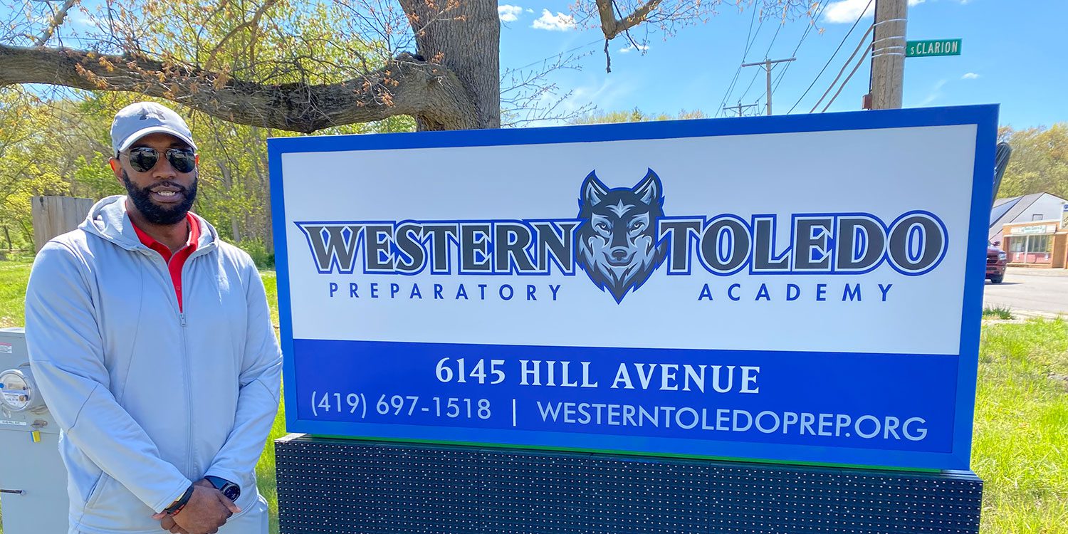 Adult next to a school sign with a wolf logo.
