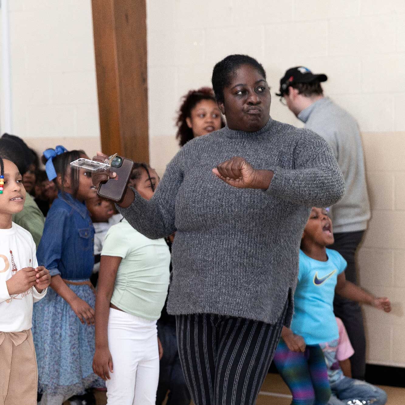 Adult gestures with a clenched fist, holding a phone, surrounded by children.