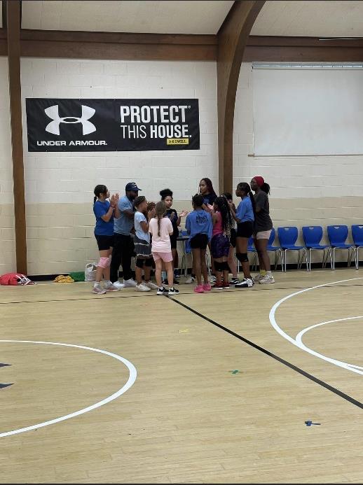 Adults and children gather in a circle on a gym floor.
