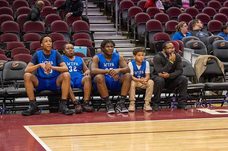 Four young basketball players and one adult sitting on a bench.