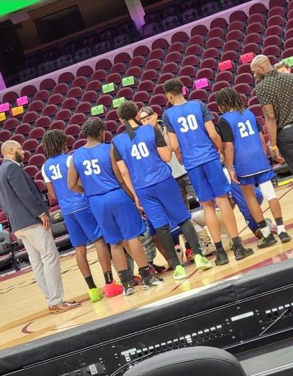 Basketball players in blue jerseys huddle on a court with two adults.