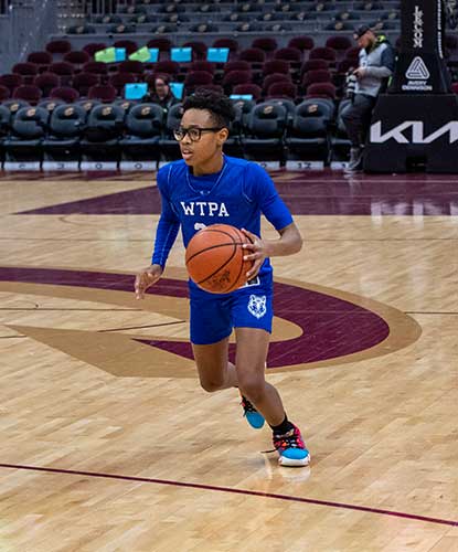 Child in blue uniform dribbling a basketball on a court.