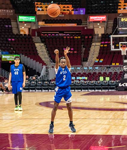 Child in blue jersey shooting basketball on court.