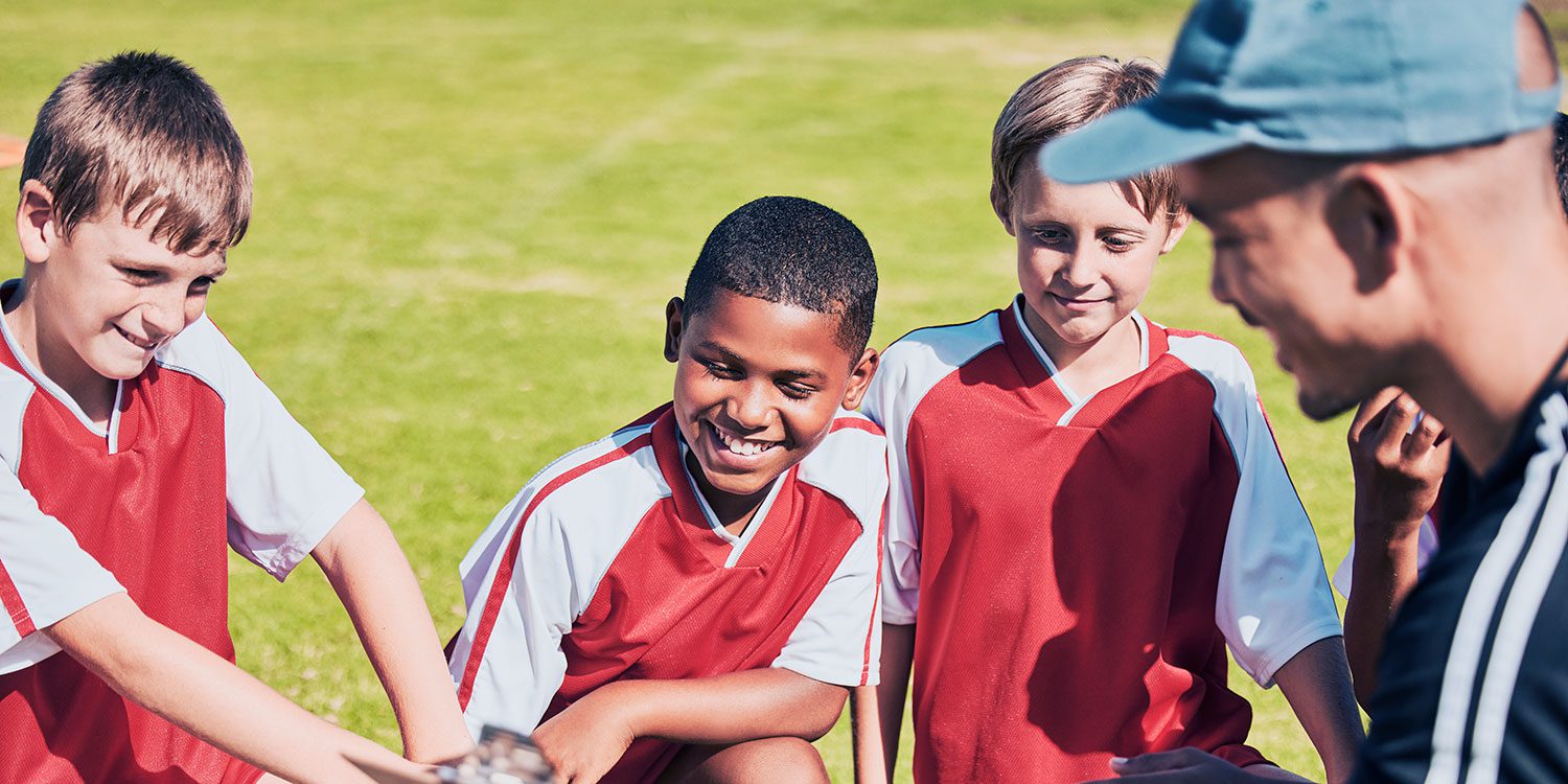 Three children in jerseys with an adult on a sports field.