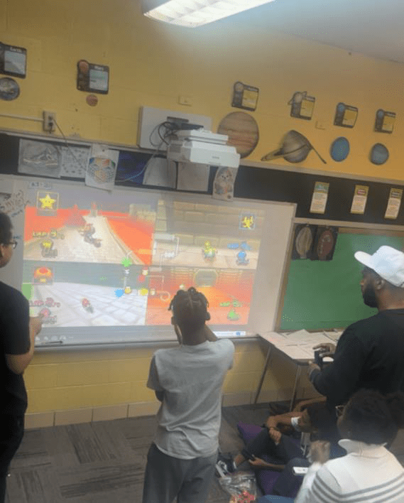 Children and adults play a video game projected on a whiteboard.