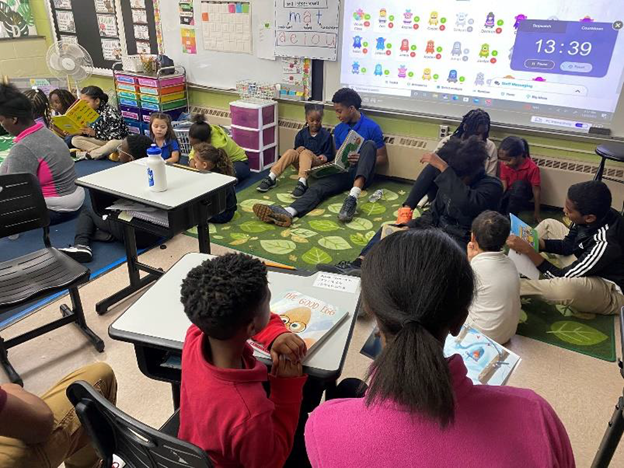 Children and adults sitting on a rug, reading books.