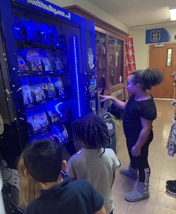 Children interact with a blue book vending machine.