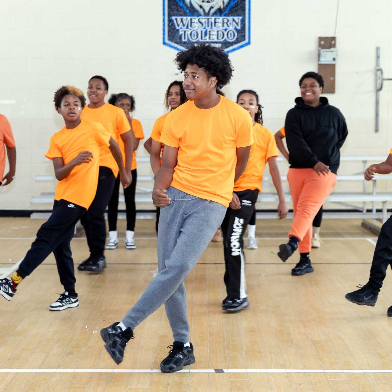 Children in orange shirts dancing on a gym floor.