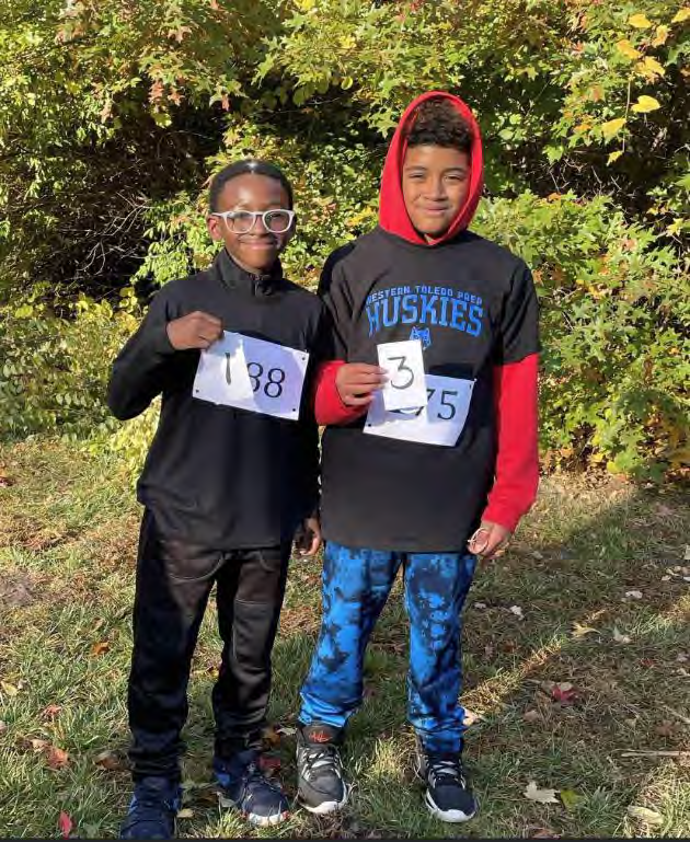 Two children smiling and holding race numbers.