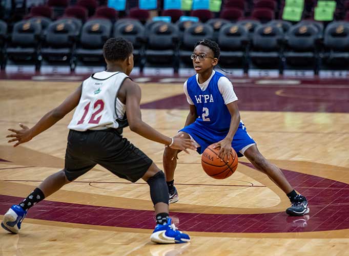 Two children playing basketball, one dribbling and one defending.