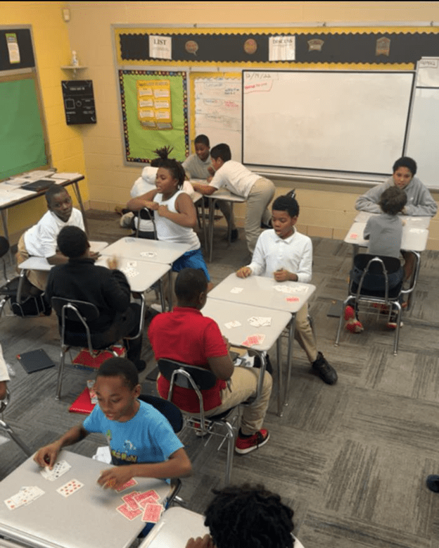 Children playing cards at desks in a classroom.