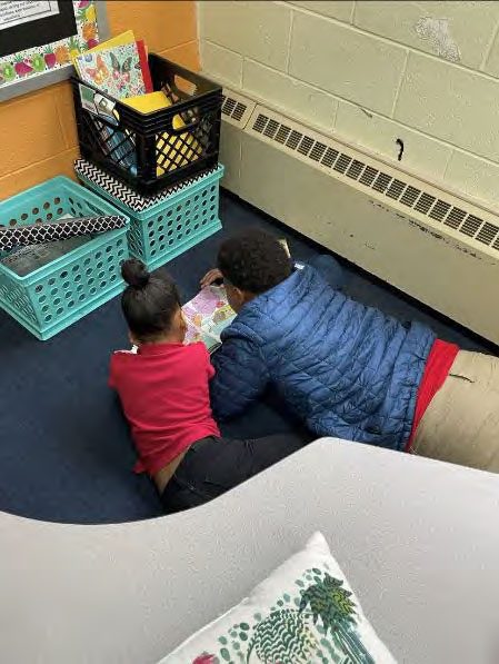 Two children lie on the floor, reading a book together.