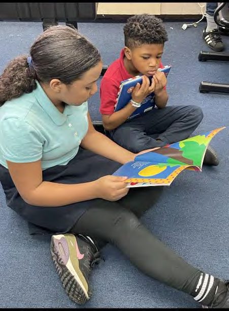 Two children sitting on the floor, reading books.