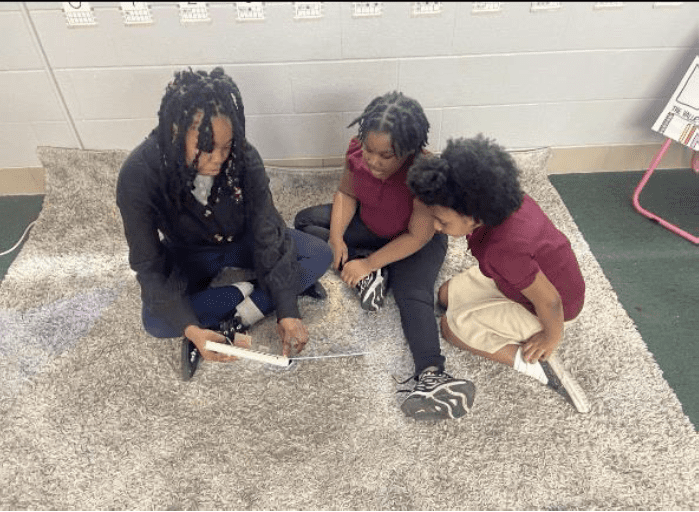 Three children sitting on a rug, looking at a book.