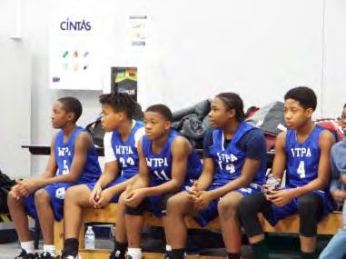 Five young adults in blue jerseys sitting on a bench.