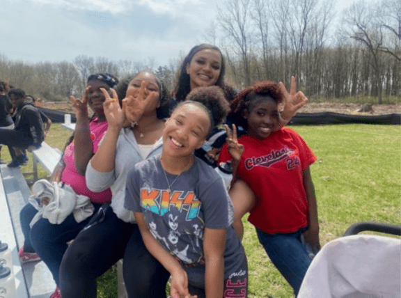Five young adults smiling and making peace signs outdoors.