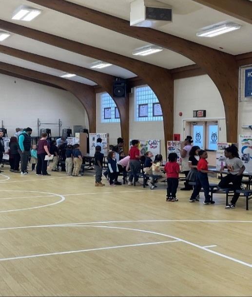Children and adults gather in a large room with display boards.